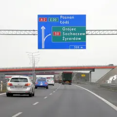 Znak drogowy informuje o minimalnej prędkości na autostradzie A2 i E30. Kierowcy zbliżają się do zjazdu na Grójec, Sochaczew i Żyrardów.