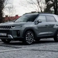Szary SsangYong Torres, nowoczesne auto z charakterystycznym grillem, zaparkowane na brukowanej ulicy.