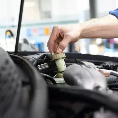 Ręka mechanika dokręca korek zbiorniczka płynu hamulcowego. Brak przeglądu może prowadzić do awarii.