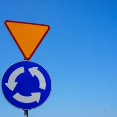 Znak ustąp pierwszeństwa i znak informujący o ruchu okrężnym na tle błękitnego nieba.