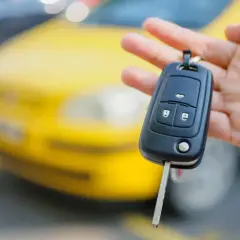 Kluczyk samochodowy z immobilizerem w dłoni, na tle żółtego auta.