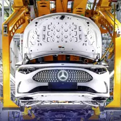 Biały samochód elektryczny Daimler na linii produkcyjnej, z otwartą maską i podświetlanym grillem z logo.