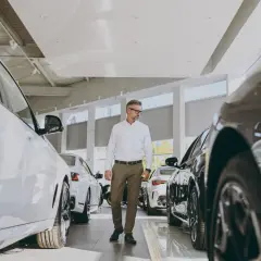 Elegancki mężczyzna w salonie samochodowym ogląda nowe, lśniące auta. Wśród nich widać kilka modeli małych samochodów, idealnych do miasta.