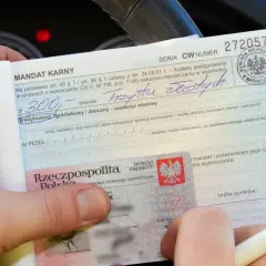Ręka trzyma mandat karny na 300 zł, obok dowód osobisty.