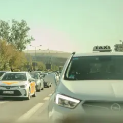 Rząd samochodów, w tym taksówek, na drodze w słoneczny dzień.