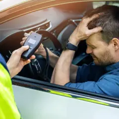 Policjant mierzy kierowcy ile promili. Mężczyzna zmartwiony trzyma się za głowę.