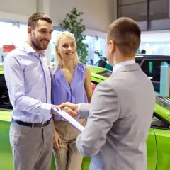 Szczęśliwa para odbiera nowe auto na e. Sprzedawca podaje im dokumenty do podpisania.