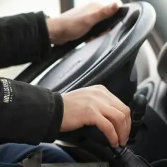Ręce kierowcy na kierownicy i drążku zmiany biegów. Na drodze obowiązuje zakaz wyprzedzania.