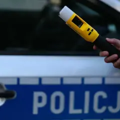 Dłoń trzyma żółty alkomat na tle radiowozu z napisem "POLICJA".