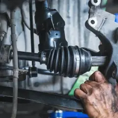 Mechanik wymienia przegub w samochodzie. Widoczny jest wałek napędowy z gumową osłoną i wielowypustem.