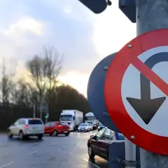 Znak drogowy zakaz zawracania na tle mokrej drogi i ruchu samochodowego.