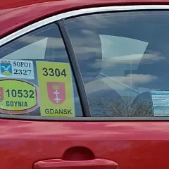 Naklejki taksówkarskie z numerami i herbami miast: Sopot, Gdynia, Gdańsk na czerwonym samochodzie.