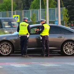 Policjanci w kamizelkach odblaskowych rozmawiają z kierowcą przy samochodzie. Może to być kontrola drogowa lub przygotowanie do odwołania od mandatu.