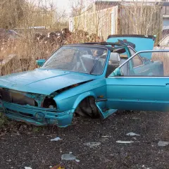 Turkusowy kabriolet czeka na demontaż. Drzwi i maska są otwarte, odsłaniając wnętrze i silnik.