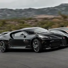 Czarny Bugatti La Voiture Noire, najdroższy samochód świata, pędzi po krętej drodze wśród wzgórz.