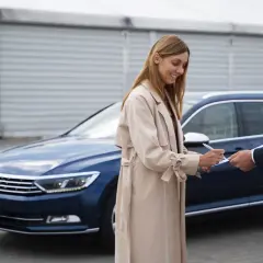 Kobieta podpisuje dokumenty przy nowym autcie, sprzedawca w garniturze podaje jej długopis.