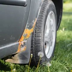 Rdza na progu samochodu, obok opony i kół, na tle zielonej trawy.