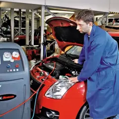 Mechanik sprawdza układ klimatyzacji w czerwonym samochodzie. Urządzenie CoolTech AC550 Pro jest gotowe do pracy, co może wpłynąć na koszt montażu klimatyzacji.