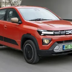 Pomarańczowe Dacia Spring, najtańsze auto elektryczne, jedzie po drodze.