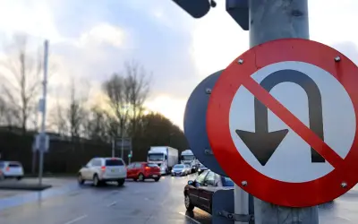 Znak drogowy zakaz zawracania na tle mokrej drogi i ruchu samochodowego.