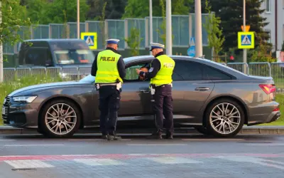 Policjanci w kamizelkach odblaskowych rozmawiają z kierowcą przy samochodzie. Może to być kontrola drogowa lub przygotowanie do odwołania od mandatu.
