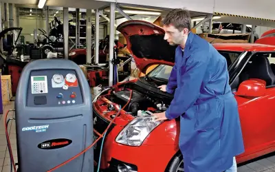 Mechanik sprawdza układ klimatyzacji w czerwonym samochodzie. Urządzenie CoolTech AC550 Pro jest gotowe do pracy, co może wpłynąć na koszt montażu klimatyzacji.