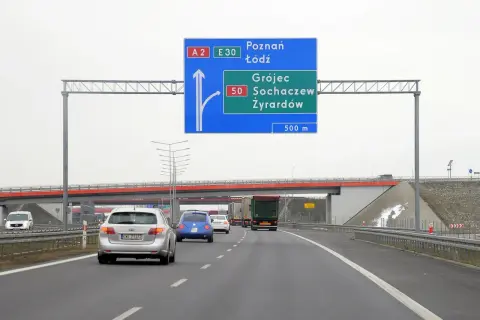 Znak drogowy informuje o minimalnej prędkości na autostradzie A2 i E30. Kierowcy zbliżają się do zjazdu na Grójec, Sochaczew i Żyrardów.