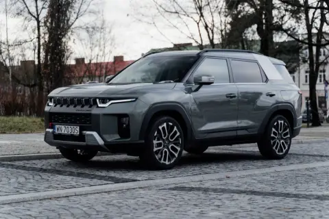 Szary SsangYong Torres, nowoczesne auto z charakterystycznym grillem, zaparkowane na brukowanej ulicy.