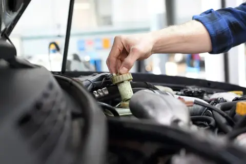 Ręka mechanika dokręca korek zbiorniczka płynu hamulcowego. Brak przeglądu może prowadzić do awarii.