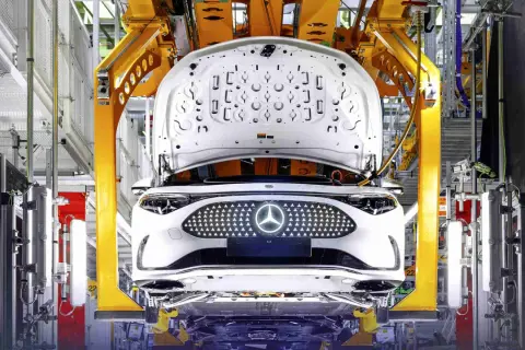 Biały samochód elektryczny Daimler na linii produkcyjnej, z otwartą maską i podświetlanym grillem z logo.