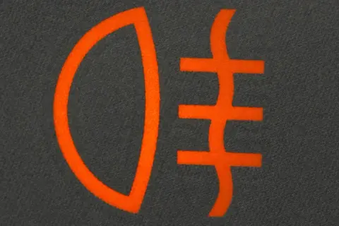 Pomarańczowy symbol świateł do jazdy dziennej na ciemnym tle.