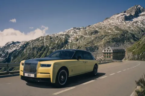 Żółty Rolls-Royce Phantom przemierza górską drogę. W tle majestatyczne szczyty i zabytkowy hotel.