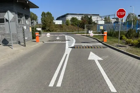 Wyraźne **znaki poziome** kierują ruch na wjeździe, gdzie szlabany i znak STOP zapowiadają kontrolę.