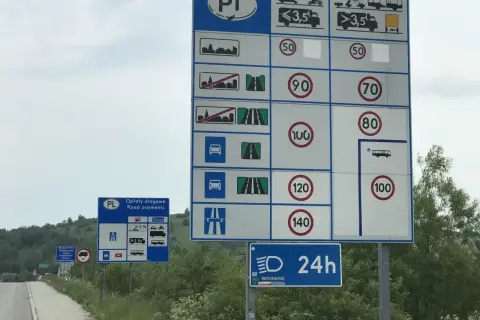 Duży znak drogowy z informacjami o opłatach i ograniczeniach prędkości. Obok mniejszy znak "Opłaty drogowe".