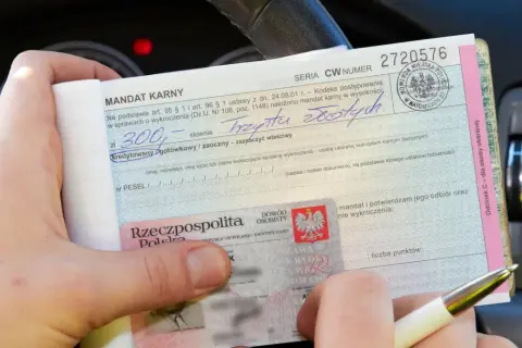 Ręka trzyma mandat karny na 300 zł, obok dowód osobisty.