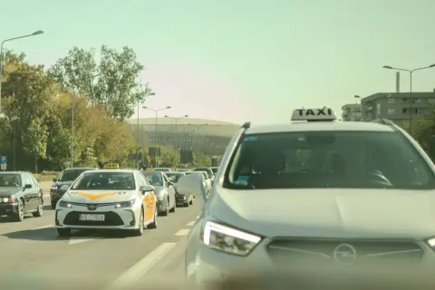Rząd samochodów, w tym taksówek, na drodze w słoneczny dzień.