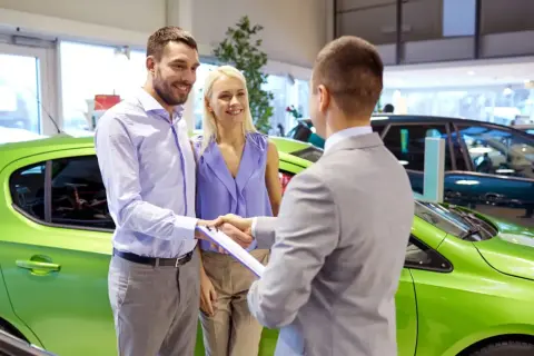 Szczęśliwa para odbiera nowe auto na e. Sprzedawca podaje im dokumenty do podpisania.