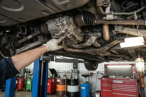 Mechanik wskazuje na skrzynię biegów w samochodzie z napędem **rwd**. Podniesiony pojazd w warsztacie.