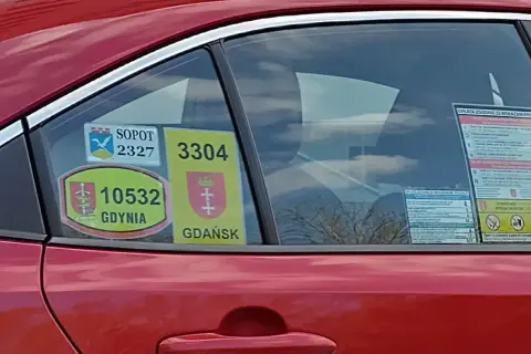Naklejki taksówkarskie z numerami i herbami miast: Sopot, Gdynia, Gdańsk na czerwonym samochodzie.