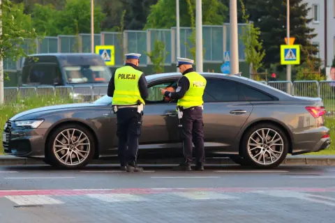 Policjanci w kamizelkach odblaskowych rozmawiają z kierowcą przy samochodzie. Może to być kontrola drogowa lub przygotowanie do odwołania od mandatu.