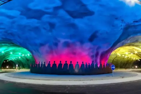 Kolorowy tunel z sylwetkami ludzi, oświetlony na zielono, różowo i żółto. To nie jest najdłuższy tunel na świecie, ale robi wrażenie.