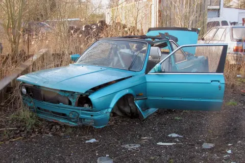 Turkusowy kabriolet czeka na demontaż. Drzwi i maska są otwarte, odsłaniając wnętrze i silnik.