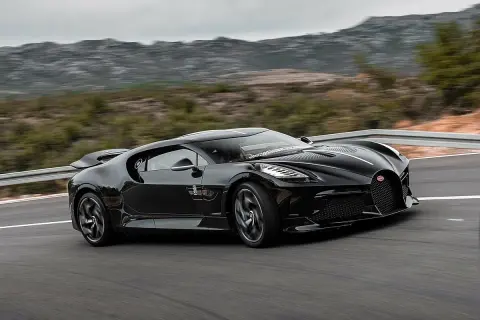 Czarny Bugatti La Voiture Noire, najdroższy samochód świata, pędzi po krętej drodze wśród wzgórz.