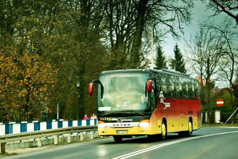 Autobus Bałtyk jedzie drogą wśród drzew.