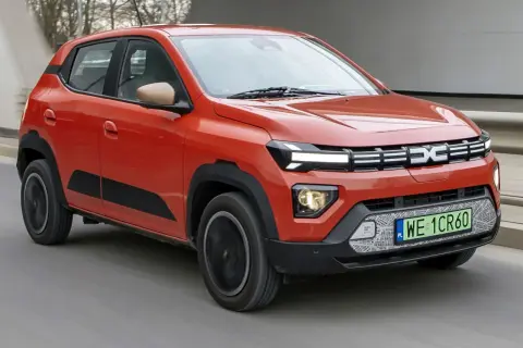 Pomarańczowe Dacia Spring, najtańsze auto elektryczne, jedzie po drodze.