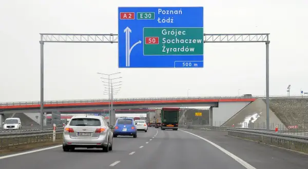 Znak drogowy informuje o minimalnej prędkości na autostradzie A2 i E30. Kierowcy zbliżają się do zjazdu na Grójec, Sochaczew i Żyrardów.