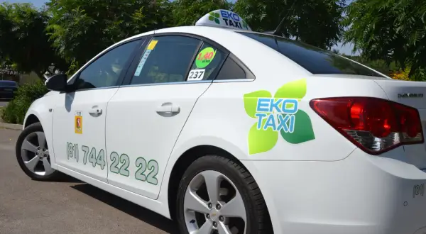 Biała taksówka EKO TAXI z zielonym logo i numerem telefonu na drzwiach.
