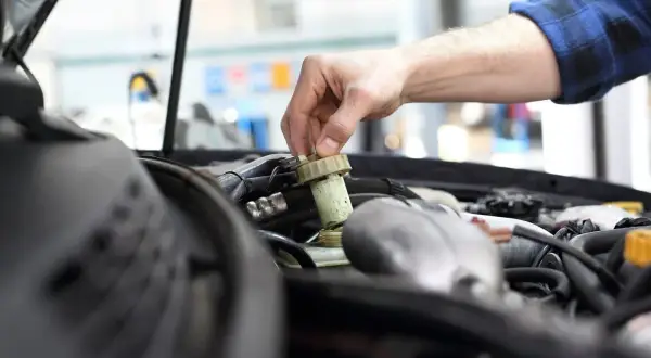 Ręka mechanika dokręca korek zbiorniczka płynu hamulcowego. Brak przeglądu może prowadzić do awarii.