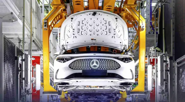 Biały samochód elektryczny Daimler na linii produkcyjnej, z otwartą maską i podświetlanym grillem z logo.