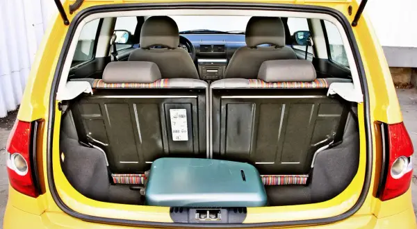 Żółty Volkswagen Fox z otwartym bagażnikiem, w którym leży zielona walizka.